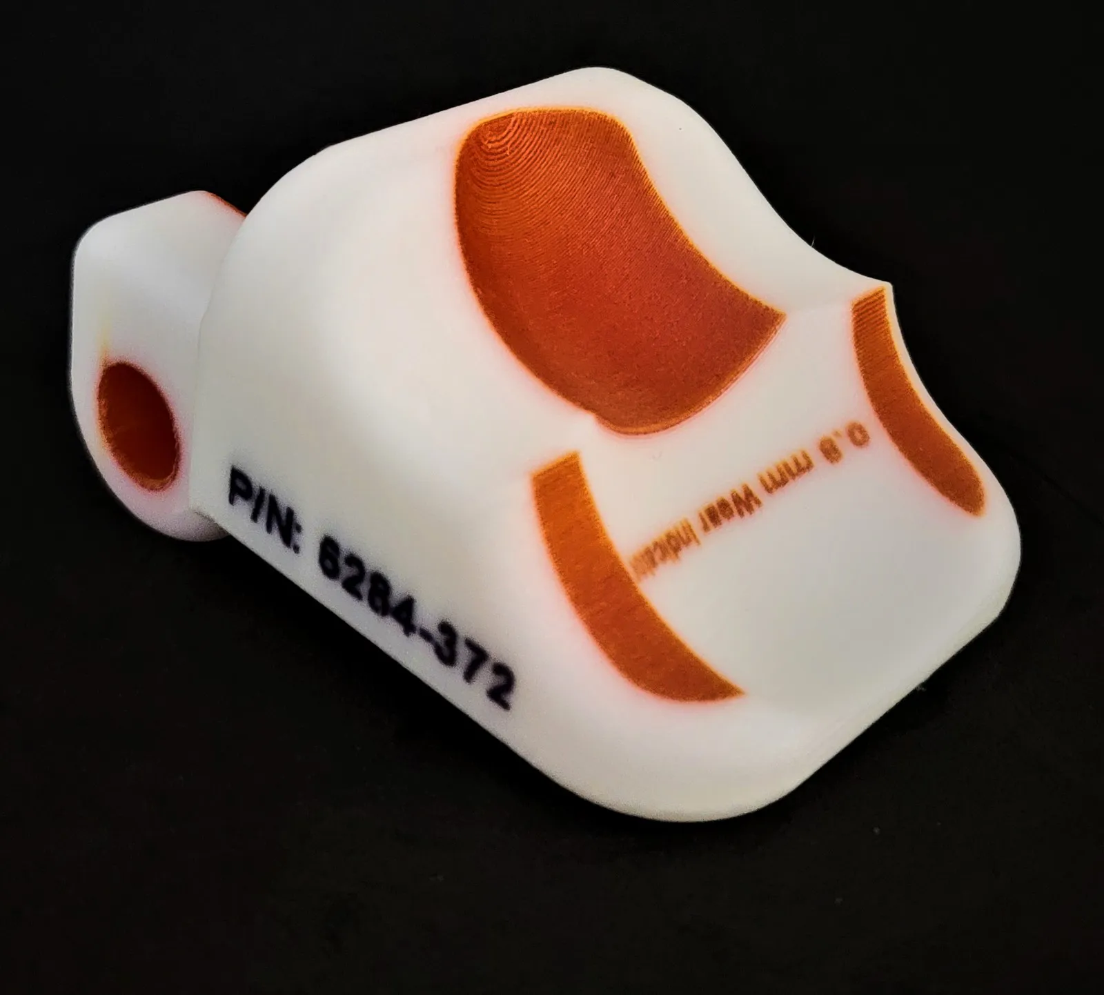 APD-printed white fixture with an orange wear-indicator layer below its contact faces and an embedded part number